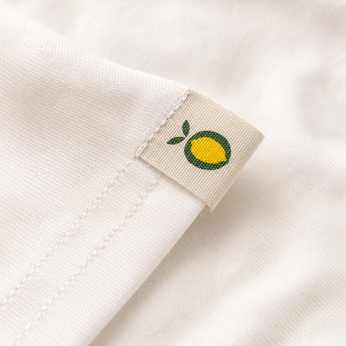 Close-up of a white ribbed crewneck sweatshirt with a visible 'NIMBÓO SUNDAYS' brand label. The graphic print at the bottom features pink vertical stripes and a yellow citrus fruit with a green leaf.